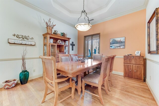 dining room featuring a raised ceiling, light wood-type flooring, and ornamental molding