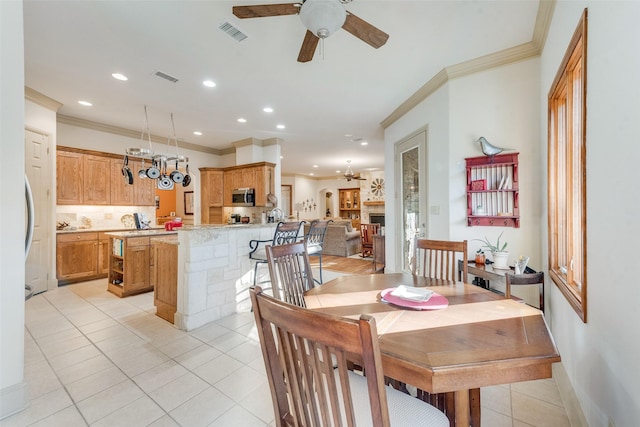 tiled dining area with ceiling fan and crown molding