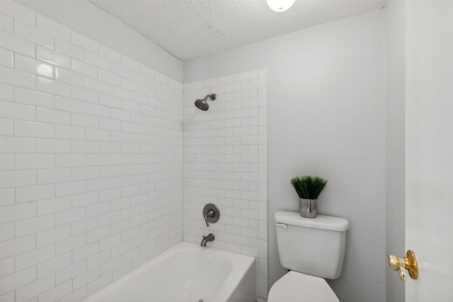 bathroom featuring a textured ceiling, toilet, and tiled shower / bath