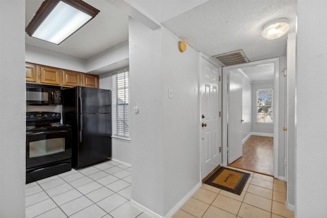 kitchen featuring light tile patterned floors, a textured ceiling, a wealth of natural light, and black appliances