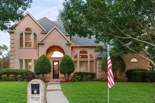 view of front of house featuring a front lawn, roof with shingles, and brick siding