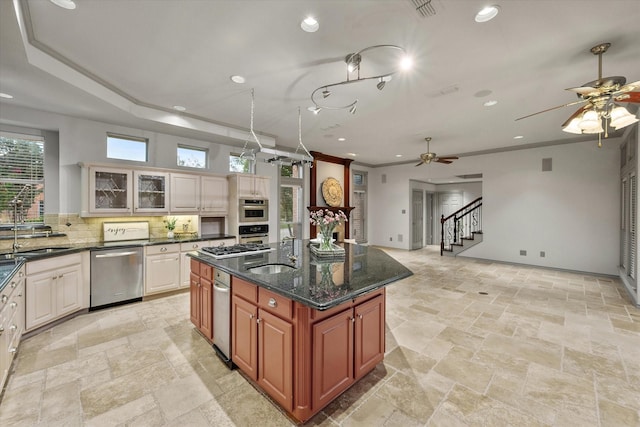 kitchen with dark stone counters, ornamental molding, stainless steel appliances, a kitchen island with sink, and decorative backsplash