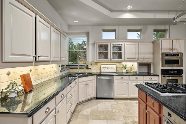 kitchen featuring sink, appliances with stainless steel finishes, dark stone countertops, white cabinets, and decorative backsplash