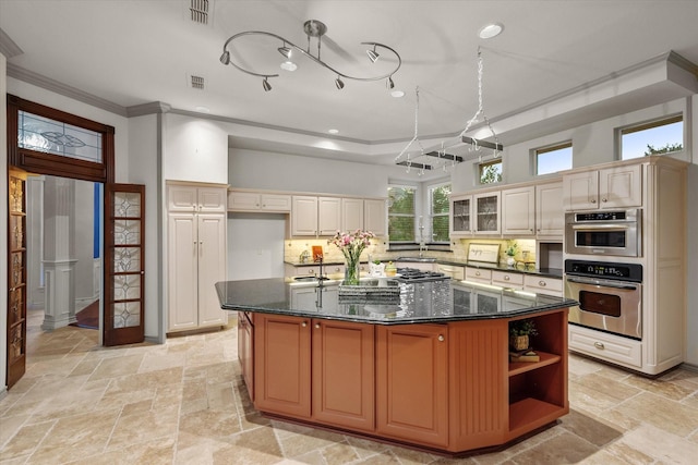 kitchen featuring ornamental molding, dark stone counters, a kitchen island with sink, and decorative backsplash