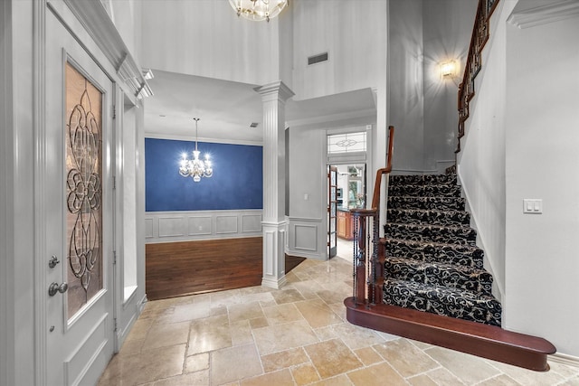 foyer entrance with ornate columns, ornamental molding, and a notable chandelier