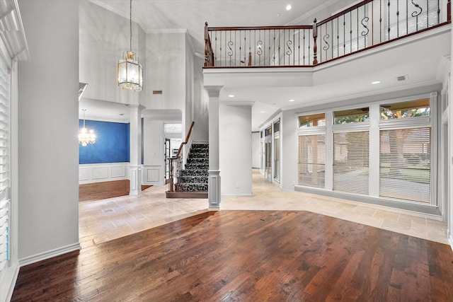 unfurnished living room featuring decorative columns, a towering ceiling, a notable chandelier, wood finished floors, and crown molding