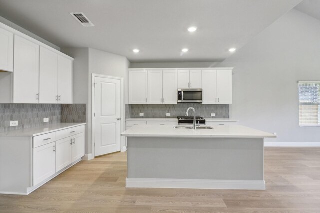 kitchen with a kitchen island with sink, sink, white cabinets, and light wood-type flooring