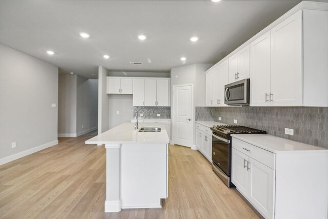 kitchen featuring appliances with stainless steel finishes, light hardwood / wood-style flooring, a kitchen island with sink, and sink