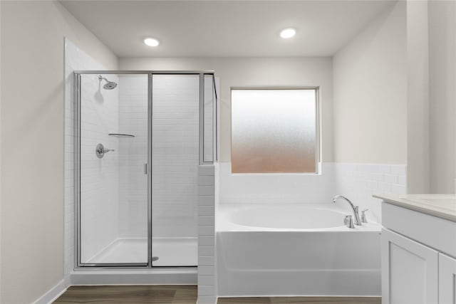 full bath featuring wood finished floors, a stall shower, a garden tub, and vanity