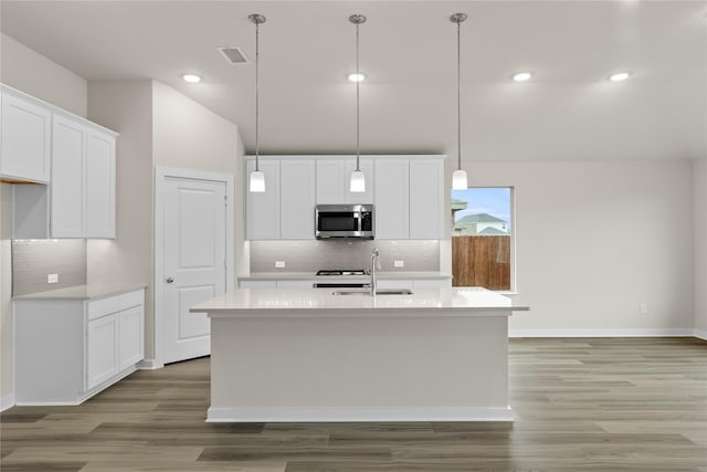 kitchen featuring light countertops, stainless steel microwave, light wood-style flooring, visible vents, and a kitchen island with sink