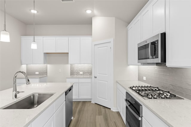 kitchen with appliances with stainless steel finishes, light wood-style flooring, a sink, and white cabinetry