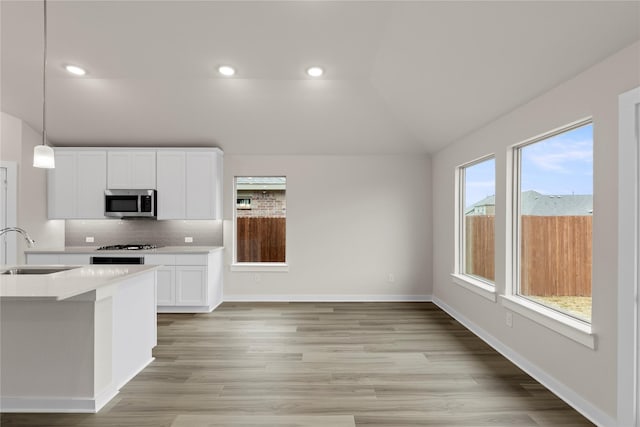 kitchen featuring tasteful backsplash, lofted ceiling, light countertops, stainless steel microwave, and a sink