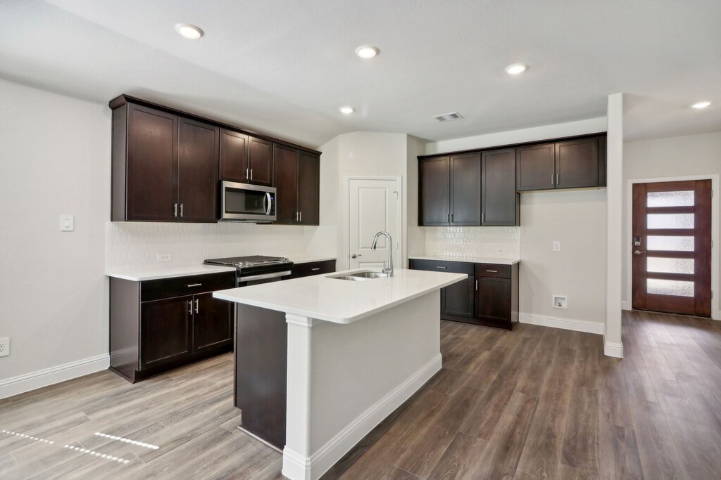 kitchen with a center island with sink, sink, hardwood / wood-style flooring, decorative backsplash, and appliances with stainless steel finishes