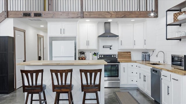 kitchen with butcher block countertops, white cabinetry, wall chimney range hood, and stainless steel appliances