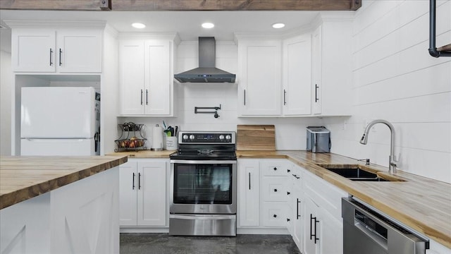 kitchen with appliances with stainless steel finishes, sink, wall chimney range hood, white cabinetry, and butcher block counters