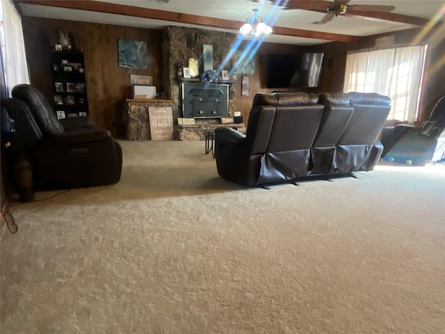 carpeted living room with beamed ceiling, ceiling fan, a wood stove, and wood walls