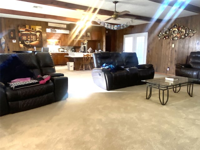 carpeted living room with beamed ceiling, ceiling fan, and wood walls