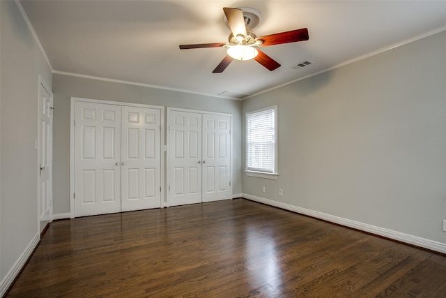 unfurnished bedroom featuring two closets, dark wood-type flooring, ornamental molding, and ceiling fan