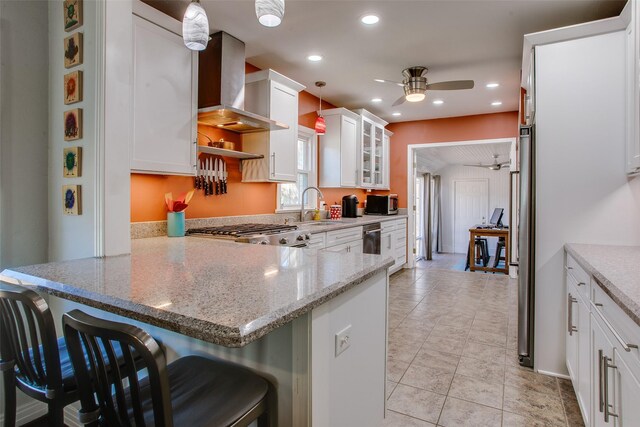 kitchen with white cabinets, hanging light fixtures, kitchen peninsula, and wall chimney exhaust hood