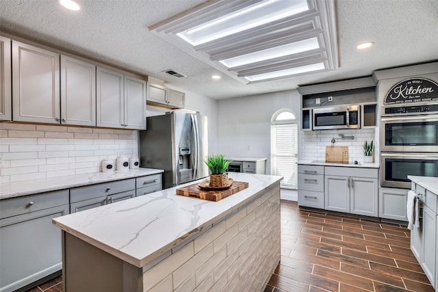 kitchen with gray cabinets, a textured ceiling, appliances with stainless steel finishes, a kitchen island, and dark hardwood / wood-style flooring