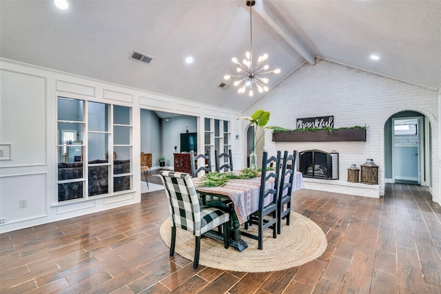 dining area with lofted ceiling with beams, a brick fireplace, dark hardwood / wood-style floors, a textured ceiling, and a notable chandelier