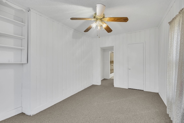 carpeted empty room featuring a textured ceiling, ceiling fan, and crown molding