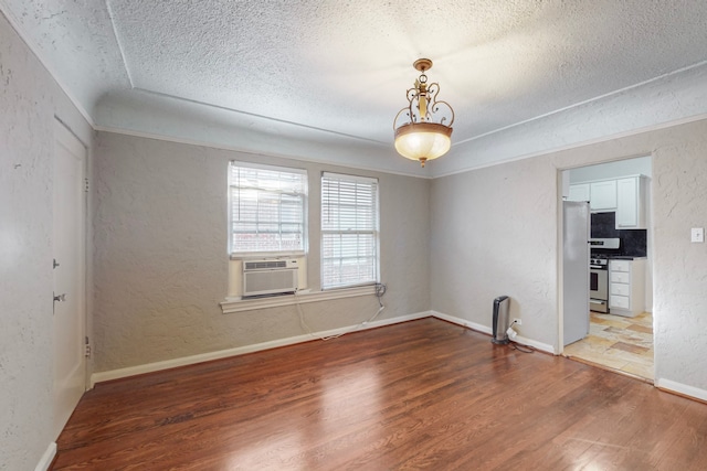 unfurnished room with hardwood / wood-style floors, a textured ceiling, and cooling unit