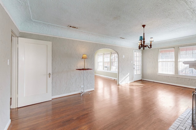 unfurnished living room with a chandelier, wood-type flooring, a textured ceiling, and a wealth of natural light