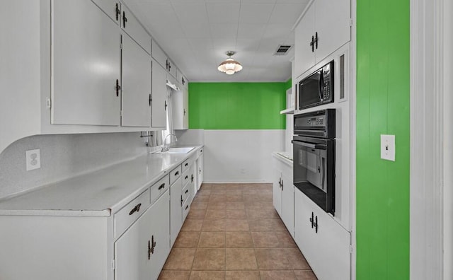 kitchen featuring sink, light tile patterned floors, black appliances, and white cabinets