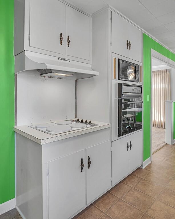 kitchen featuring white cabinets, oven, light tile patterned floors, and white stovetop