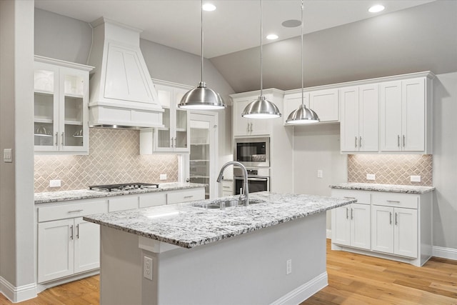 kitchen with custom exhaust hood, lofted ceiling, a center island with sink, sink, and white cabinetry