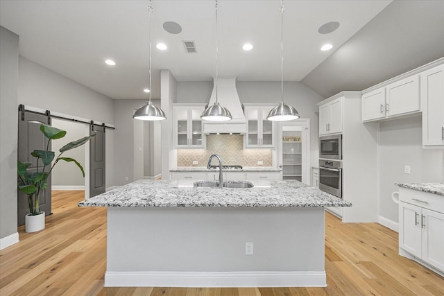 kitchen with a barn door, light hardwood / wood-style flooring, hanging light fixtures, and appliances with stainless steel finishes