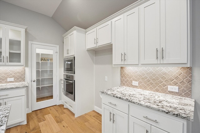 kitchen featuring backsplash, white cabinets, vaulted ceiling, light stone countertops, and light wood-type flooring