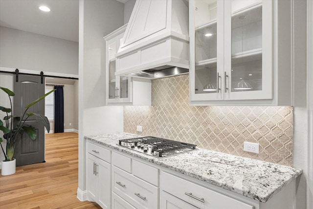 kitchen with premium range hood, stainless steel gas cooktop, a barn door, light hardwood / wood-style flooring, and white cabinets