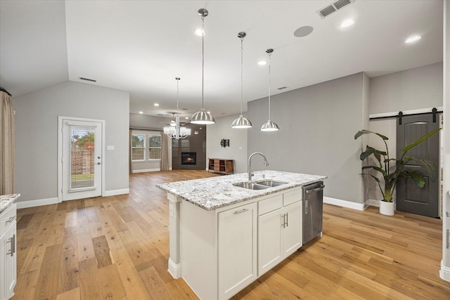 kitchen with sink, dishwasher, light hardwood / wood-style floors, hanging light fixtures, and an island with sink