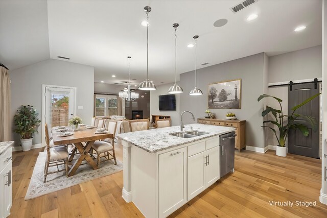 kitchen with sink, a barn door, light hardwood / wood-style floors, decorative light fixtures, and a center island with sink