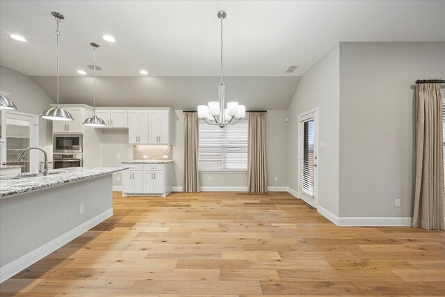 kitchen with stainless steel microwave, sink, light hardwood / wood-style flooring, light stone countertops, and white cabinetry