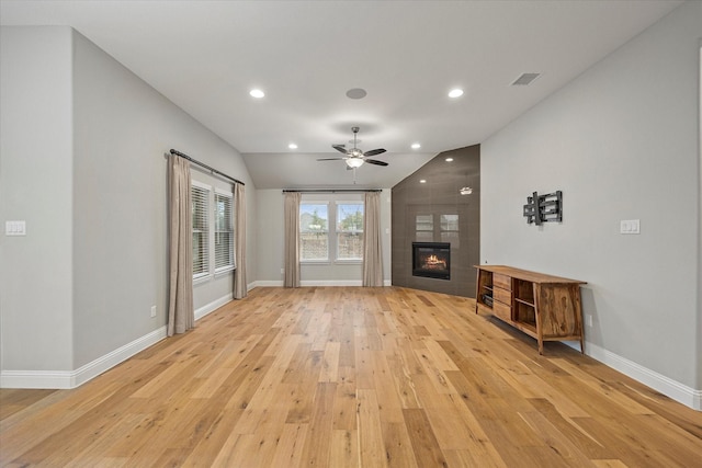 unfurnished living room with ceiling fan, a tiled fireplace, lofted ceiling, and light hardwood / wood-style flooring