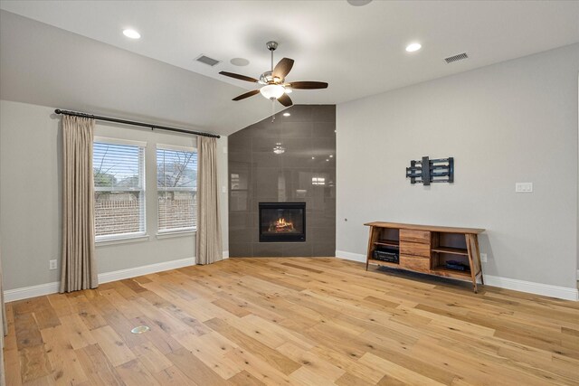 unfurnished living room with a tile fireplace, ceiling fan, light hardwood / wood-style flooring, and vaulted ceiling