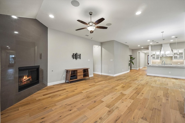 unfurnished living room with lofted ceiling, sink, ceiling fan, a fireplace, and light hardwood / wood-style floors