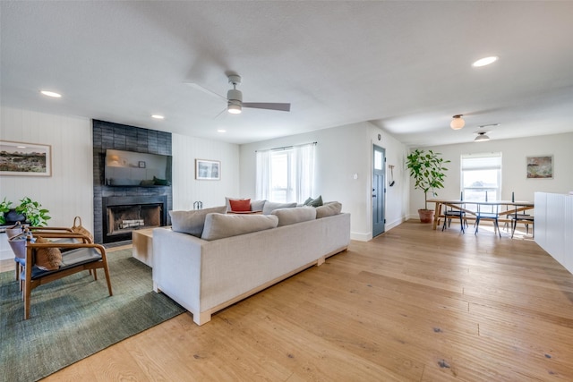 living room with ceiling fan, a fireplace, and light hardwood / wood-style floors