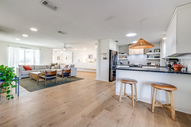 kitchen featuring decorative backsplash, stainless steel fridge with ice dispenser, dark countertops, light wood-type flooring, and open shelves