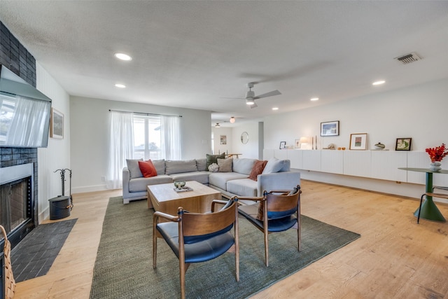 living room featuring a fireplace, a textured ceiling, light hardwood / wood-style floors, and ceiling fan