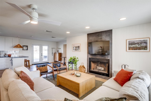 living room with a large fireplace, ceiling fan, french doors, and light wood-type flooring