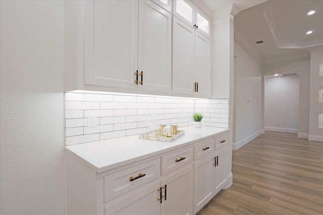 bar featuring backsplash, white cabinets, crown molding, light stone countertops, and light wood-type flooring