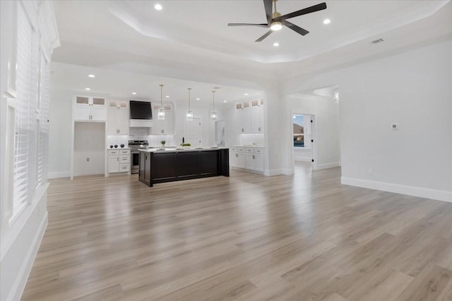 unfurnished living room with a tray ceiling, ceiling fan, and light wood-type flooring