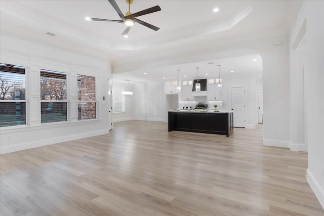 unfurnished living room featuring light hardwood / wood-style floors, ceiling fan, and a tray ceiling