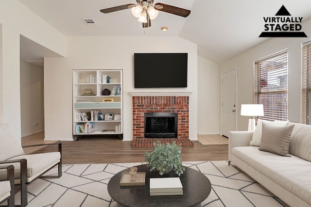 living room featuring light hardwood / wood-style flooring, a fireplace, lofted ceiling, and ceiling fan