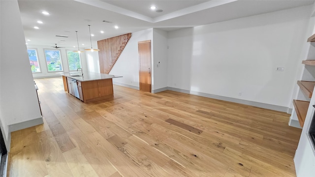 kitchen with light wood-type flooring, ceiling fan, sink, decorative light fixtures, and a center island with sink