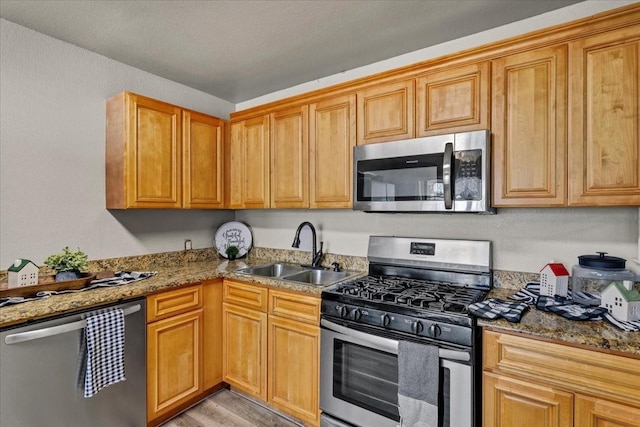 kitchen with light hardwood / wood-style floors, sink, appliances with stainless steel finishes, and dark stone counters